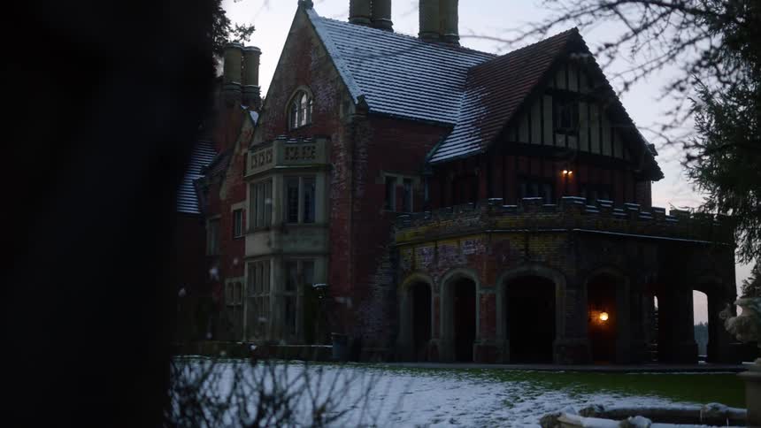 A light dusting of snow covers the ground in front of a large house