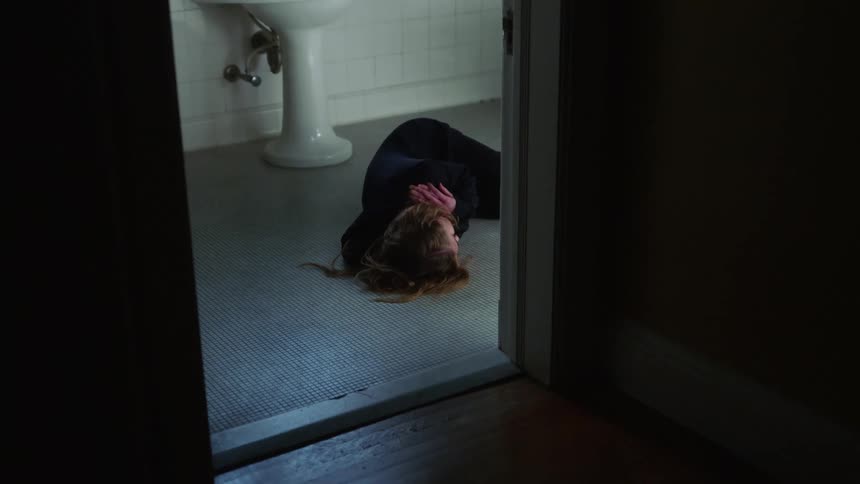 A woman laying on the bathroom floor next to a doorway and a sink