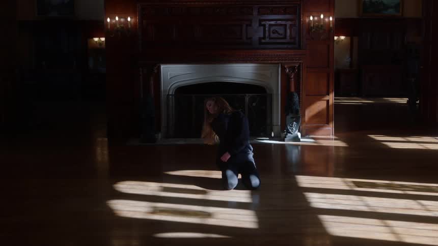 A teenage girl kneeling in front of a fireplace at home rolls her body around and clenches at her throat