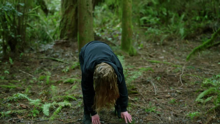 Woman spins around on forest ground then stands