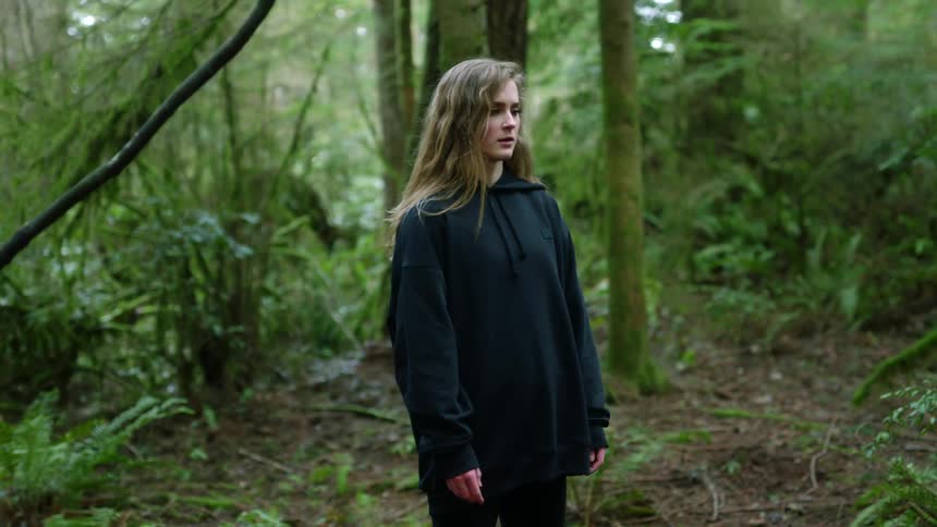 Blonde girl with a black hoodie stands in the green woods