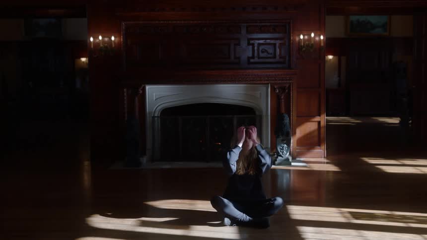 Woman performs dance routine in large room with fireplace containing wooden floor