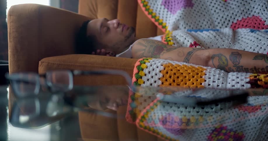 A tattooed man sleeps on a sofa in house during the day