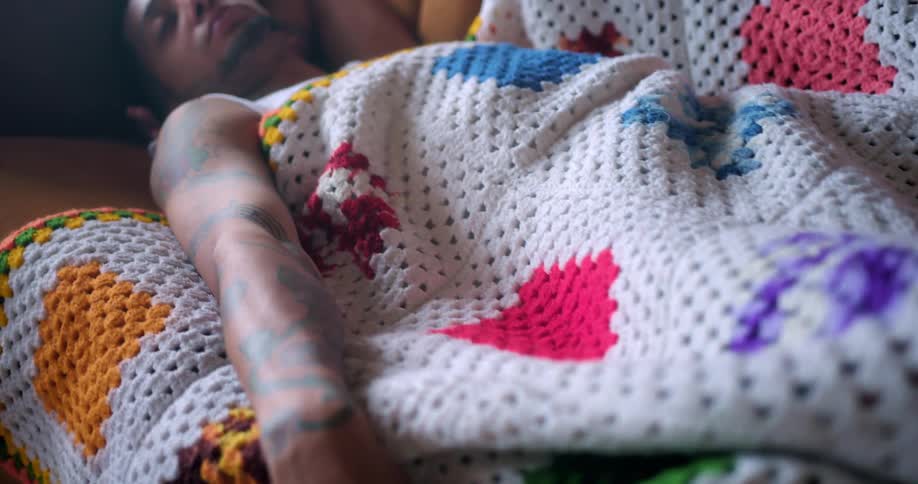 A young man sleeps under a blanket on a sofa during the day