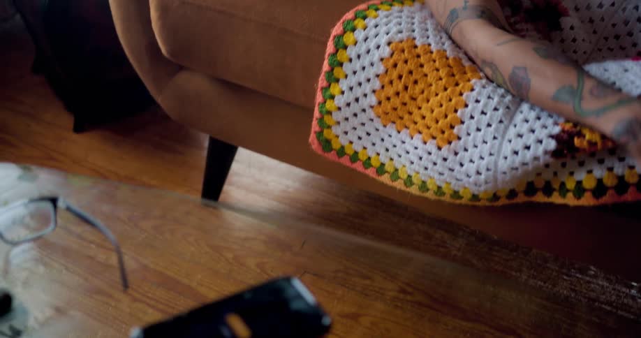 A man sleeping on the couch reaches over and touches his cell phone on a table