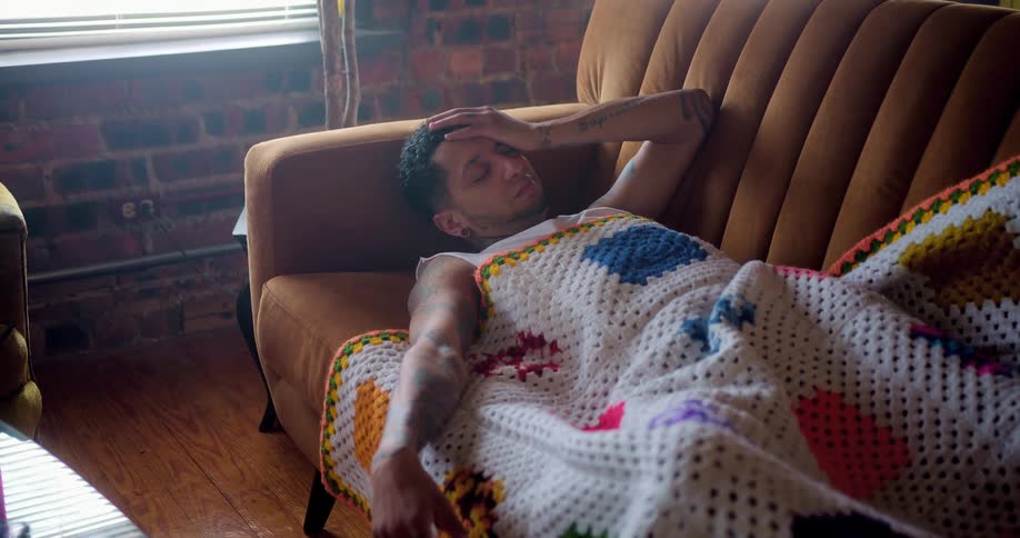 Tattooed man sleeping on the sofa wakes up and checks his smartphone in the living room