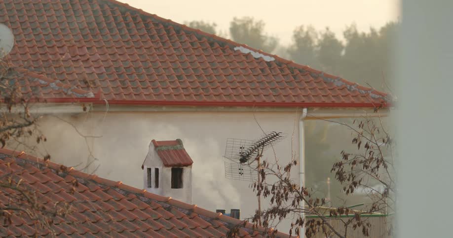 Smoke rises from small chimney on house with tile roof in early morning