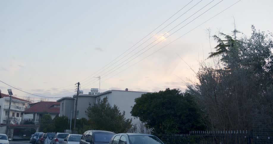 A neighborhood with vehicles a utility pole buildings and the sky in the background