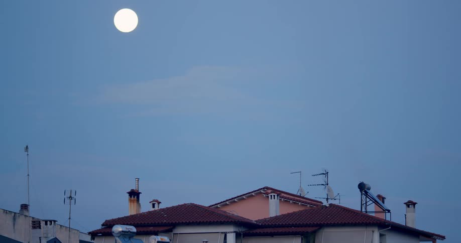 A full moon glowing above building rooftops