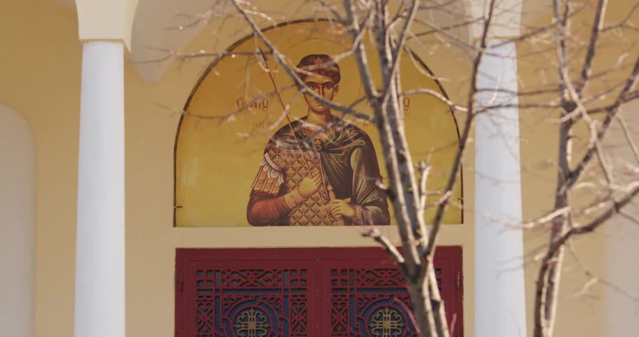 A church with a door with a picture of a saint above with a tree in the foreground