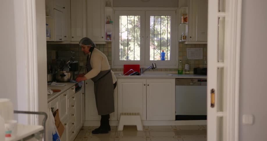 A woman wipes her kitchen counter while wearing an apron
