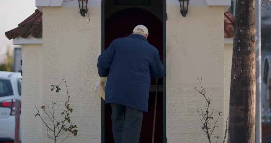 Elderly man with a cane walking up to his front door