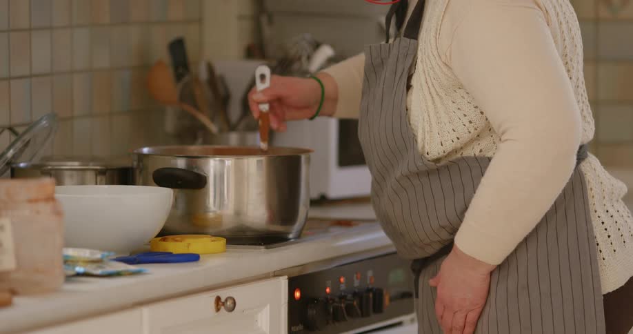 Woman stirs large pot on stove in kitchen