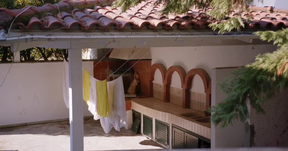 Yellow and white clothing are hung out to dry on a patio under a stucco roof