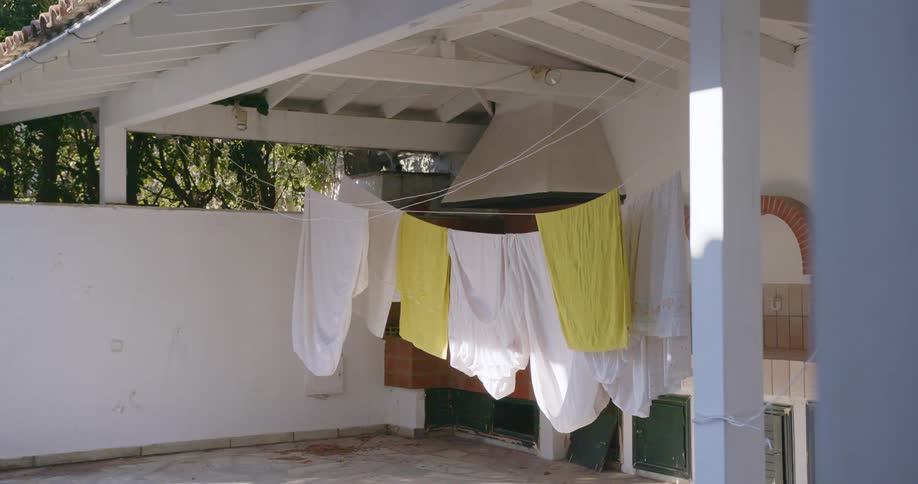 Laundry dries on clothe line strung in open air structure near trees