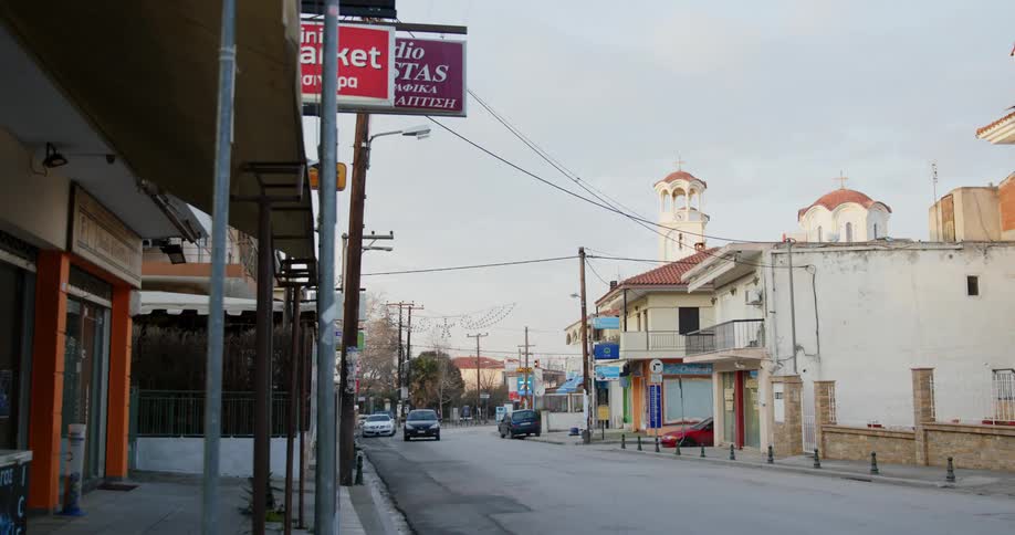 A person walks out of a store on a quiet street as a car drives down it