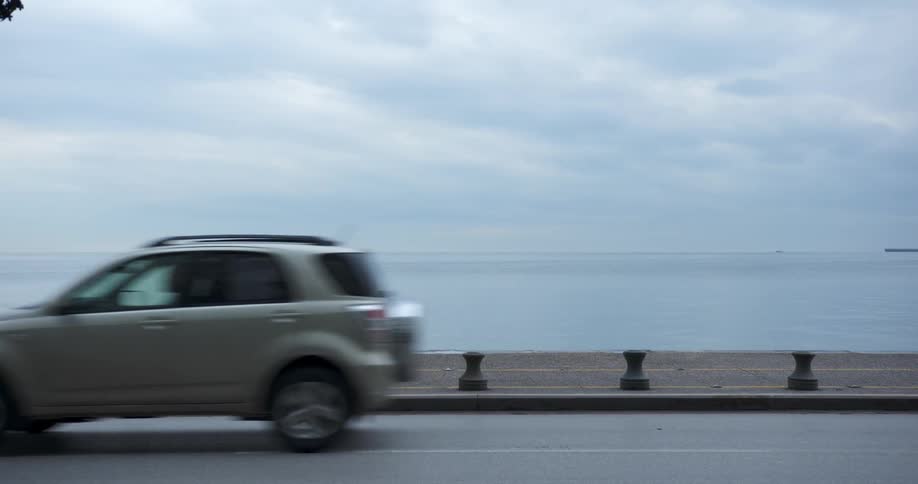 Traffic and pedestrians travel along a road on the coast on a cloudy day