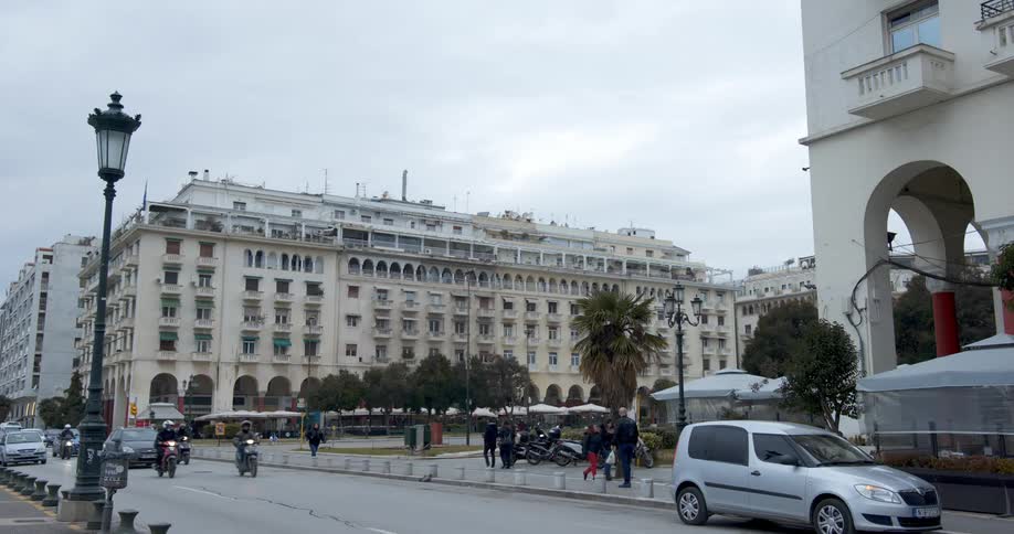 Traffic and pedestrian travel along a road next to a large building in a city during the day