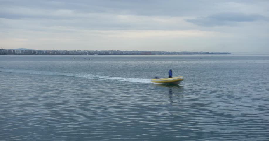 A boater rides a motorboat on the ocean away from a metropolis on a cloudy day