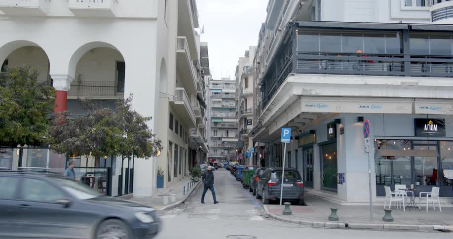 Pedestrians cross street toward cafe on corner as traffic flows past