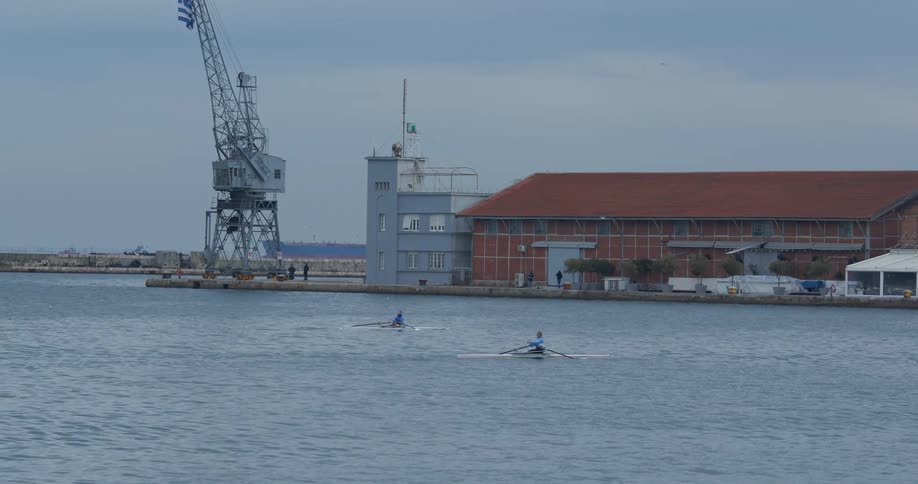 People rowing boats past a building on the shore