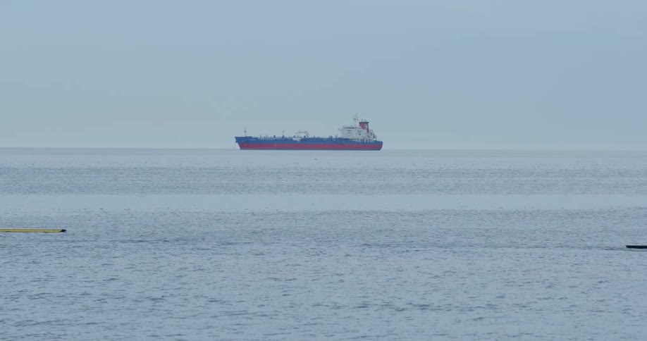 Person rows boat in across ocean while haze covers freighter near the horizon