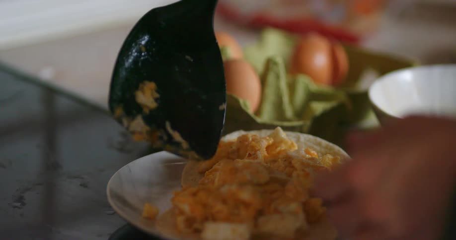 Person puts scrambled eggs on tortillas with spatula