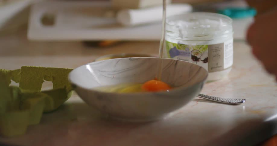 A person cracks an egg into a small dish