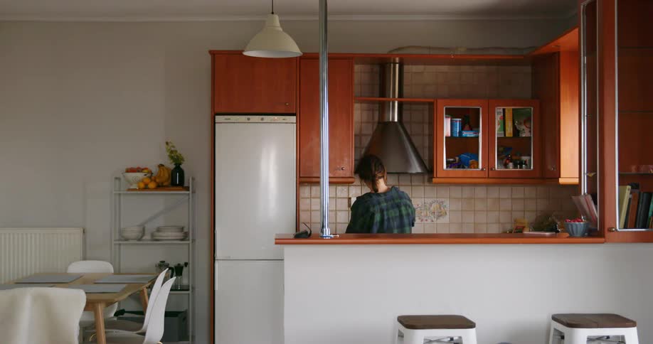 A woman washes dishes in a small kitchen during the day