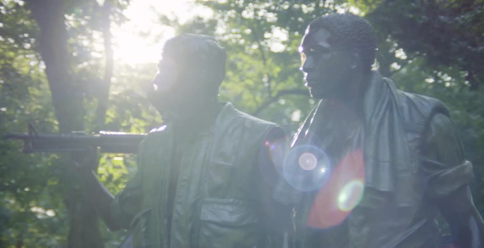 A statue of three Vietnam War soldiers with trees leaves the sky and clouds in the background
