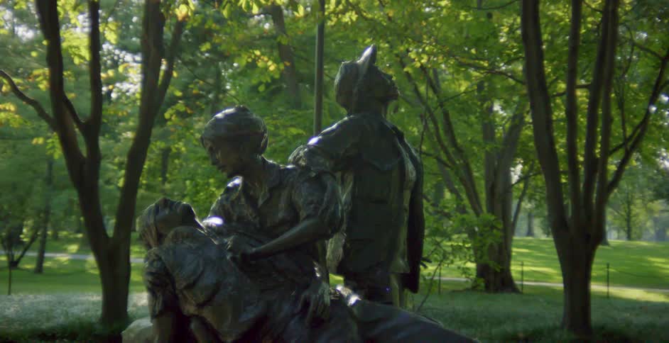 A sculpture of a woman cradling a wounded man in a public park during the day