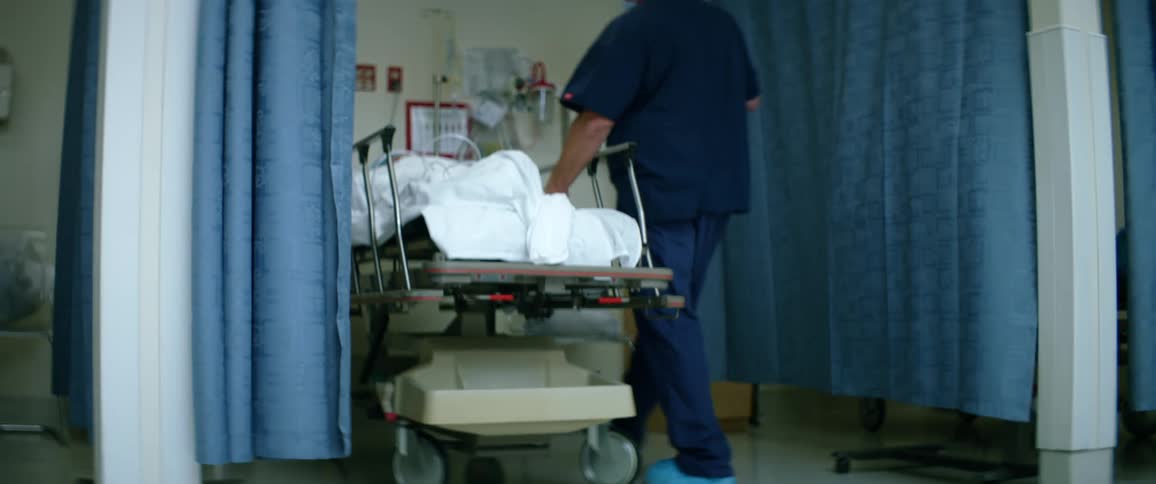 A nurse approaches a patient lying on a stretcher and removes the bed sheet covering them