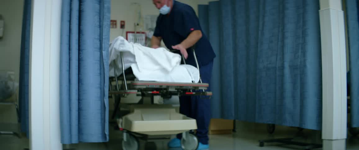 A nurse straightens out the bedding on a wheeled bed in an emergency room