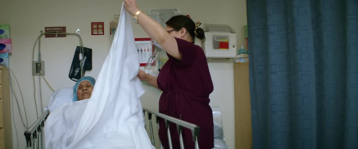 A female nurse fixes a blanket over a patient in a hospital bed