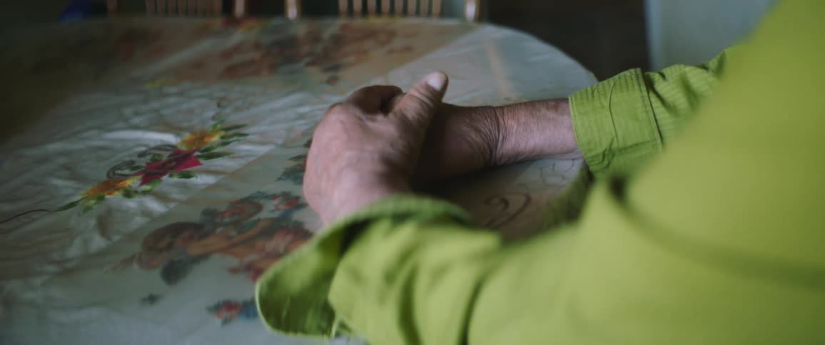 An elderly woman sits at home and rubs her hands together