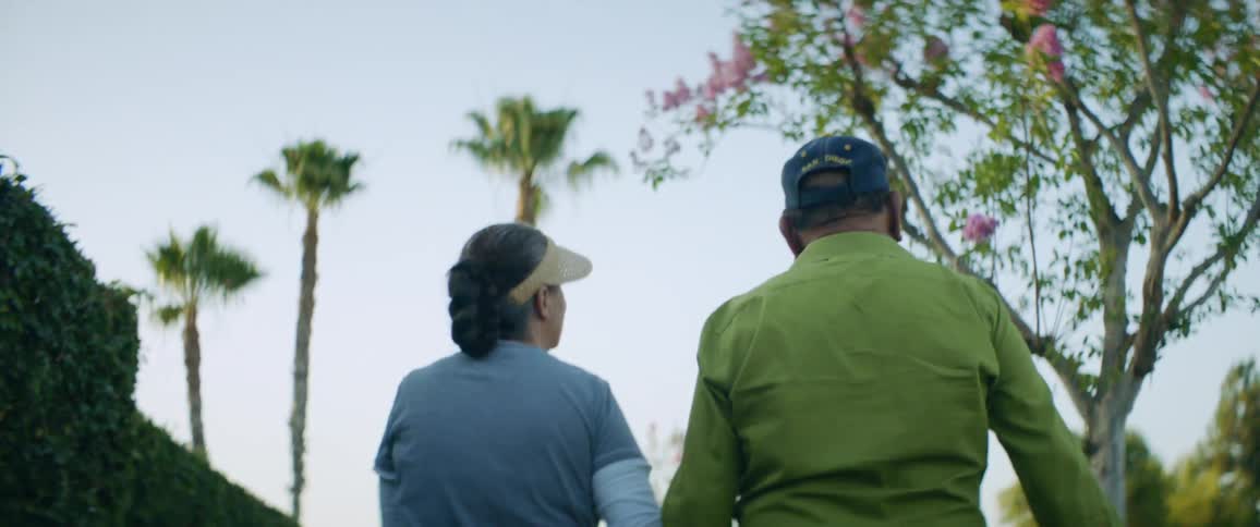A husband and wife hold hands as they walk through a neighborhood