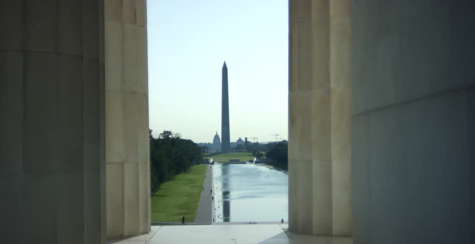 People walk around a man made pond in front of a monument in a city