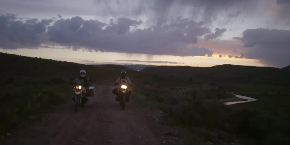 Two people ride motorcycles down a dirt road