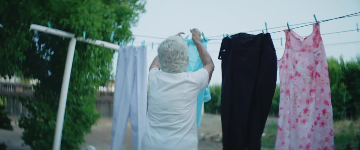 An elderly woman hangs laundry on a clothesline outside