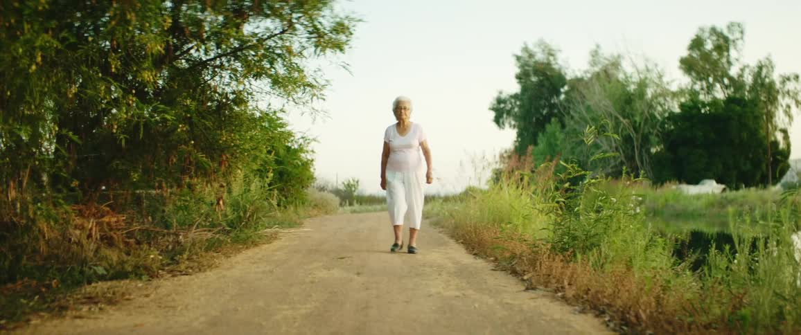 Elderly woman walks down dirt path in countryside
