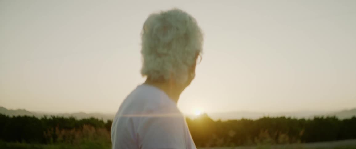Elderly woman with grey hair and a pink shirt watches sunset