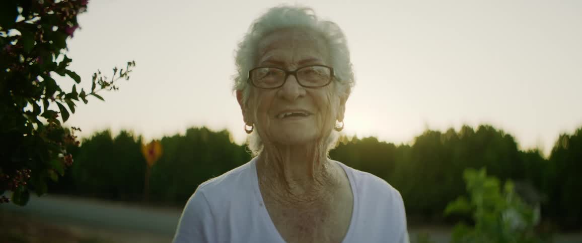 Elderly woman poses as she touches flowering tree near road