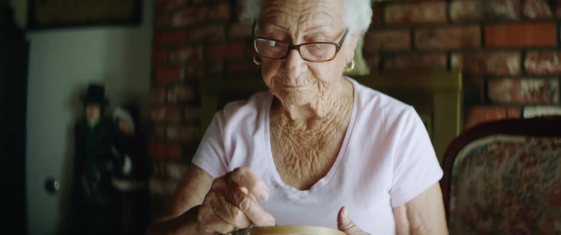 A woman with glasses sitting in a room with a wall in the background