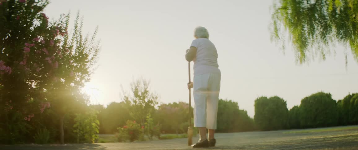 An elderly woman sweeping outside