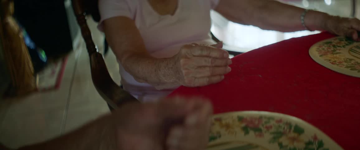 People sitting at table with red table cloth hold hands