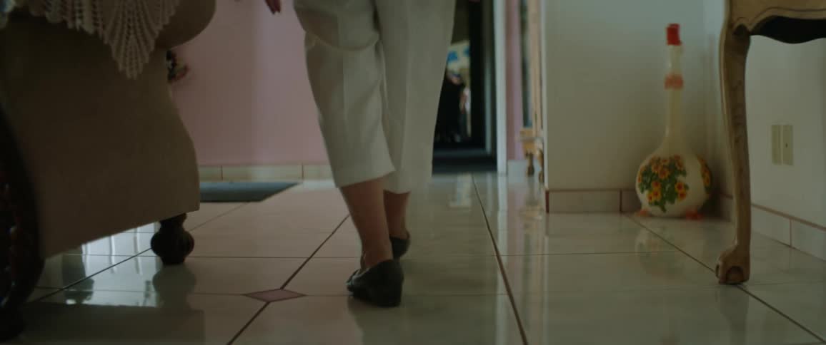 A person walking in a room with a couch and with a mirror in the background