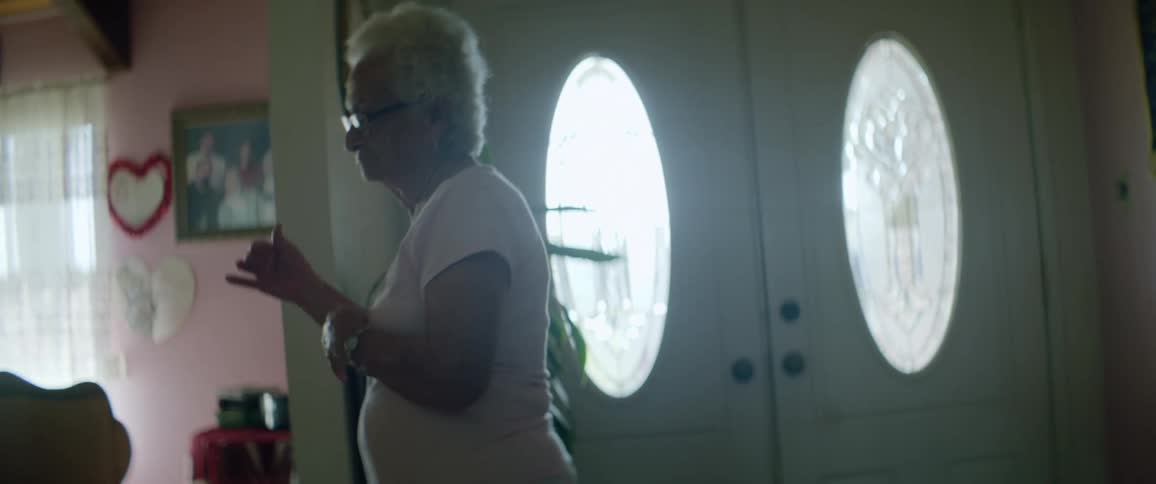 Elderly woman with short grey hair and glasses dances own her own in a room