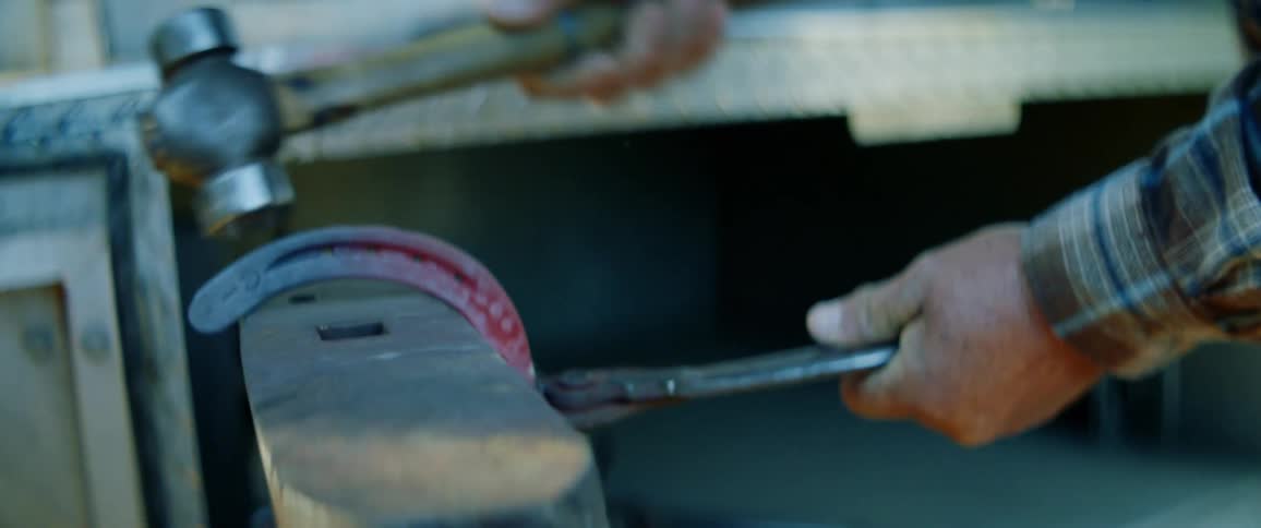 A man hammers a hot horse shoe