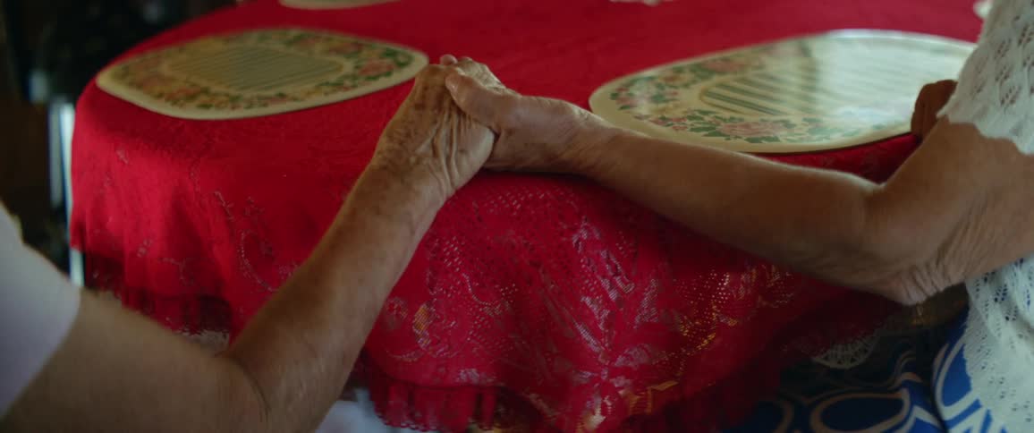 An elderly couple holds hands while sitting at a dining table