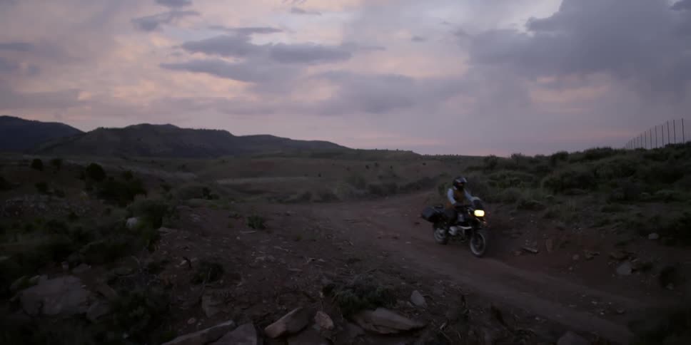 Two people ride motorcycles down a dirt trail